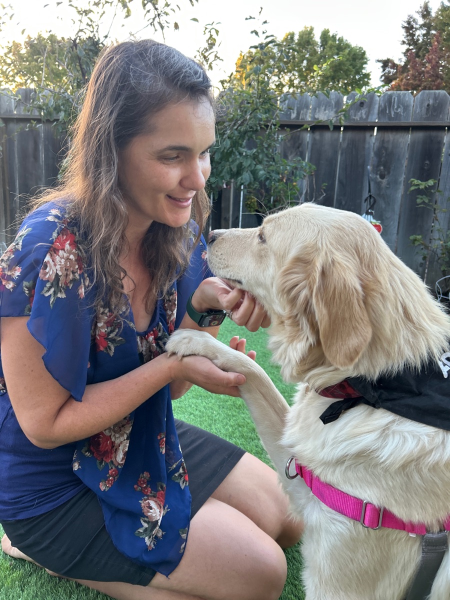 Georgia holding a golden retriever's paw in the backyard